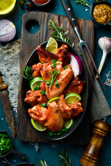 Wall Mural - Fried chicken wings with lime, rosemary and onions. In a black plate. On a dark background.