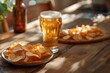A glass of beer and a plate of chips sit on a wooden table