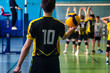 © Alex Vog - Rear view of guy in black yellow sportswear uniform with 10 number at active match. Team volleyball game, volleyball court in sport school gym. Sports games, team success concept. Copy ad text space