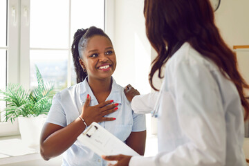 Wall Mural - Black woman doctor or nurse is talking with a happy patient in a hospital. The atmosphere is one of genuine care, with the medical professional engaging in a conversation.