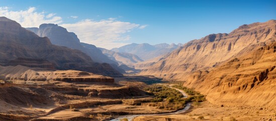 Canvas Print - A river flows through a valley nestled among towering mountains, creating a picturesque natural landscape under the vast sky and drifting clouds