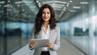 © MP Studio - A young businesswoman stands in an office with a tablet in her hands.