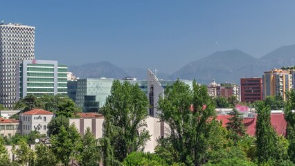 Wall Mural - Cityscape over Tirana with its colorful apartment buildings and skyscrapers timelapse, Tirana, Albania. Aerial view from viewpoint of pyramid with green trees and mountains