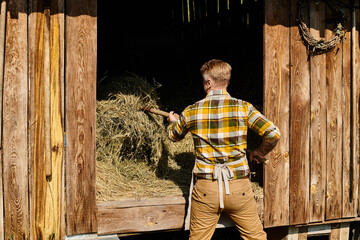 appealing dedicated farmer in casual attire using pitchfork while working with hay in village