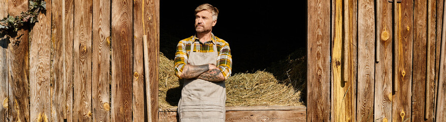 good looking farmer in casual attire using pitchfork while working with hay in village, banner