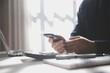 © Phanphen - Side view shot of a man's hands using smart phone in interior, rear view of business man hands busy using cell phone at office desk, young male student typing on phone sitting at wooden table, flare