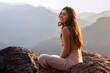 © ADDICTIVE STOCK - A joyful woman sits basking in the golden light of sunrise on a mountain peak, with a stunning backdrop of misty mountains