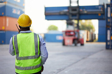 back view African worker or engineer using walkie talkie and showing gesture to crane car in containers warehouse storage