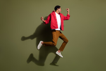 Wall Mural - Full length photo of positive carefree man dressed red shirt jumping high rising fists empty space isolated green color background
