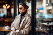 © Garnar - Stylish caucasian white woman in beige trench coat and designer eyewear enjoys coffee. Poise adding to the serene vibe of an outdoor cafe. Concept of quiet luxury, sophisticated elegance. Copy space