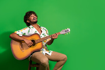 Poster - Photo portrait of pretty young male sit chair sing play guitar dressed stylish citrus print outfit isolated on green color background