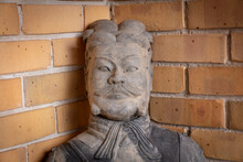 Photograph Of The Face And Head Of A Terracotta Soldier Imitation Statue Against A Brown Brick Wall In An Urban Dwelling