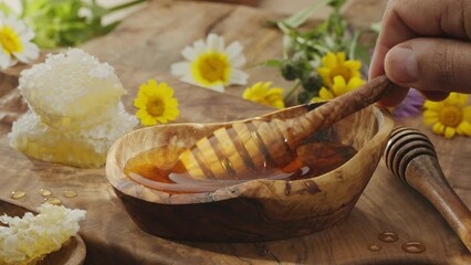 Wall Mural - Drops of honey slowly flowing from a wooden honey dipper into a honey bowl, close-up, slow motion. A perfect food background for any of your projects.