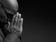 © herlanzer - man praying to god with hands together on grey black background with people stock image stock photo