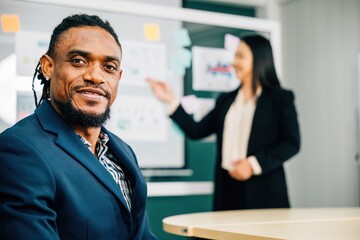 Wall Mural - In an office meeting, a black businessman, a charismatic CEO and leader, smiles at the camera. His presence exudes confidence and success. A portrait of leadership and diversity in a corporate setting