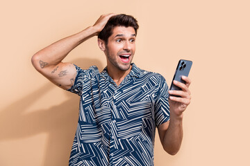 Aufkleber - Portrait of impressed funny guy wear stylish shirt astonished staring at smartphone arm on head isolated on beige color background