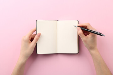 Wall Mural - Woman writing in notebook on pink background, top view