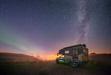 Night shot of a painted camper van under the Milky Way with northern lights, Gimsoy, Lofoten, Nordland, Norway, Europe