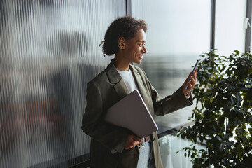 Wall Mural - a woman is standing in front of a window holding a laptop and a cell phone