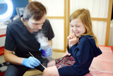 Fototapeta Tulipany - A caring doctor checks moles on the skin of a small child. Dermatologist remove of benign tumors with liquid nitrogen for cute preschooler girl. Baby fears of treat.