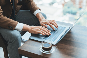 Top view of smart businessman hand searching, typing,analyzing data by using laptop. Closeup image of manager hands working with laptop on wooden desk with coffee cup surrounded by nature. Ornamented.