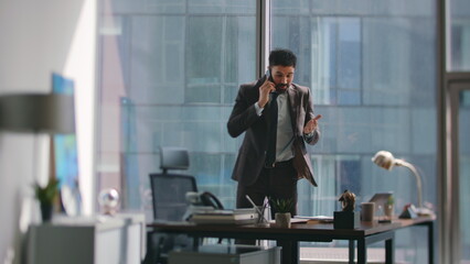 Employee frustrated phone call standing office looking business documents.