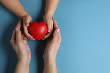 Wall Mural - Mother and her child holding red decorative heart on light blue background, top view. Space for text