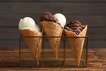 Wall Mural - Tasty ice cream scoops in waffle cones on wooden table, closeup