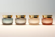 Four jars of makeup with gold caps inside present subtle color gradations, streamlined design, muted tonality