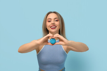 Poster - Beautiful young woman with blue sweet macaroon heart shaped gesture on color background