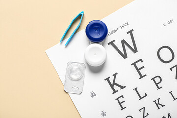 Wall Mural - Eye test chart with tweezers, container and contact lens on beige background