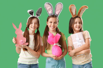 Cute little girls with Easter bunny ears, gifts and decor on green background