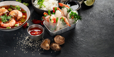 Wall Mural - Traditional Asian food table. Spring roll, rice, shrimp, sushi, vegetables, meat on dark background