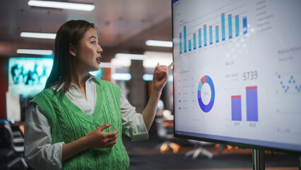 Creative Office Meeting: Portrait of Beautiful Asian Female Project Manager Presenting Goals For Marketing Strategy, Uses TV Set with Data Analysis, eCommerce Infographics