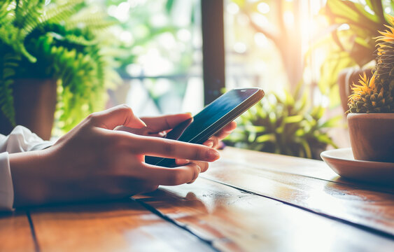 A young woman holding a smartphone sitting at the table. A mockup, a phone, a smartphone. Close-up hands, copy space, bokeh effect in the background.