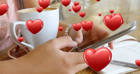 Wall Mural - Close up of a pair of female hands texting beside a cup of coffee and a pen and notebook