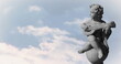 Image of gray sculpture of cupid over blue sky and clouds, copy space