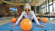 Energetic senior lady in yoga pose with fitness ball at a gym.