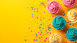 Festive delicious home-baked cupcakes with colorful pastel icing and sprinkles. Top down view and isolated on a bright yellow background with copy space.