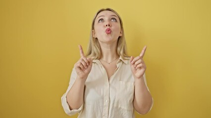 Sticker - Amazed young blonde woman joyfully pointing up, looking surprised on isolated yellow background, expressing cheerful confidence