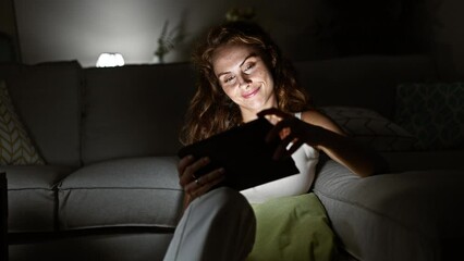 Canvas Print - A serene woman enjoys reading on her tablet in a cozy living room at night.