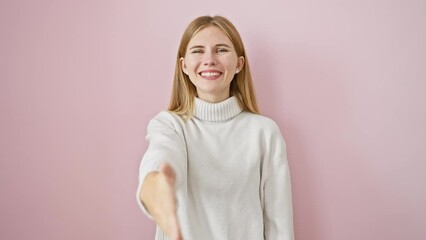 Canvas Print - Beautiful blonde girl offering friendly business handshake, greeting with a smile. standing successful over pink isolated background.