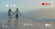Couple holds hands on beach, viewed on a camera in 4K record mode.