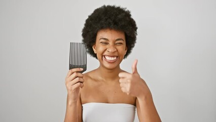 Wall Mural - Young african american woman wearing towel holding comb smiling happy and positive, thumb up doing excellent and approval sign over isolated white background