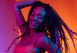 © Sascha - A black woman with long braids dancing and smiling  in a studio with neon light.