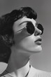 Black and white side view photography of a brunette young woman with rounded sunglasses looking up at the sun in summer, vintage 1960s style fashion model girl portrait