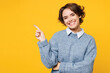 © ViDi Studio - Young smiling happy woman she wears grey knitted sweater shirt casual clothes point index finger aside on workspace area mock up isolated on plain yellow background studio portrait. Lifestyle concept.