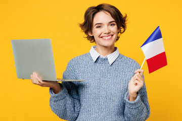 Wall Mural - Young IT woman wears grey knitted sweater shirt casual clothes hold French flag use work on laptop pc computer chatting online isolated on plain yellow background studio portrait. Lifestyle concept.