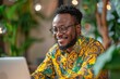 © Georgii - Focused businessman in a vibrant shirt working on a laptop in a green office space