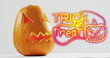 Neon trick or treat text banner with pumpkin icon over halloween pumpkins against grey background